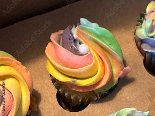 Pastel frosted cupcake with swirled buttercream and sugar pearl displayed in bakery case among other cupcakes.