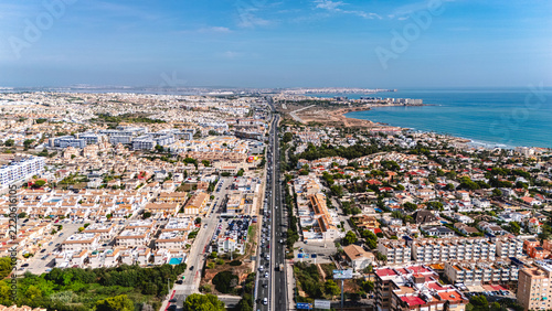 Aerial panorama of coastal highway through residential districts towards Torrevieja in Alicante, Spain, under a clear blue sky. Coastal development, Mediterranean tourism and suburban infrastructure