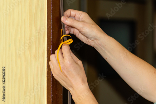 Hand using tools to press rubber insulation tape on a door frame