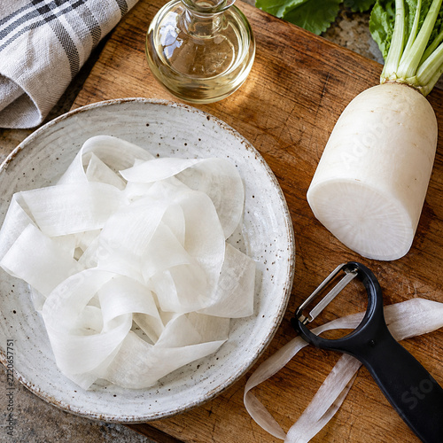 Thin radish ribbons beside a safe resting vegetable peeler