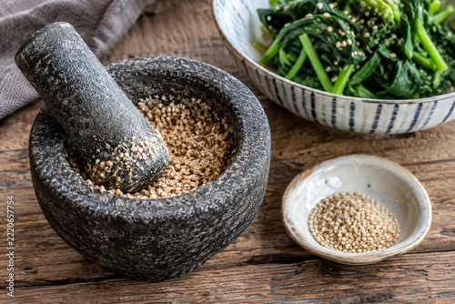 Sesame seeds in a small mortar beside a bowl of greens