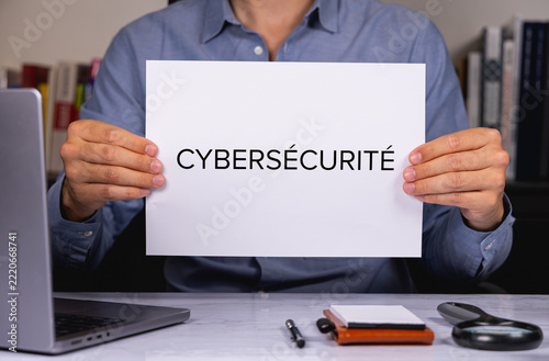 Une personne en chemise tenant une feuille de papier sur laquelle est écrit en gros le mot cybersécurité.