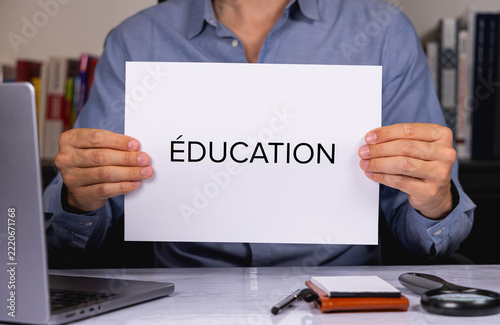 Une personne en chemise tenant une feuille de papier sur laquelle est écrit en gros le mot éducation.