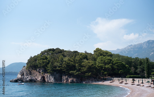 Scenic pebble beach curves along a calm, turquoise bay next to a lush, pine-covered rocky headland in Montenegro