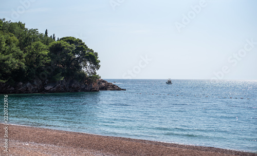 Scenic view of a pebble beach and clear turquoise sea near a forested rocky headland