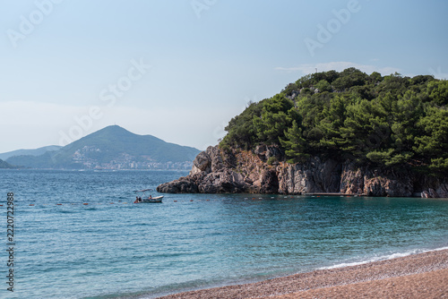 Small motorboat floats on the calm turquoise sea near a rocky, pine-covered headland