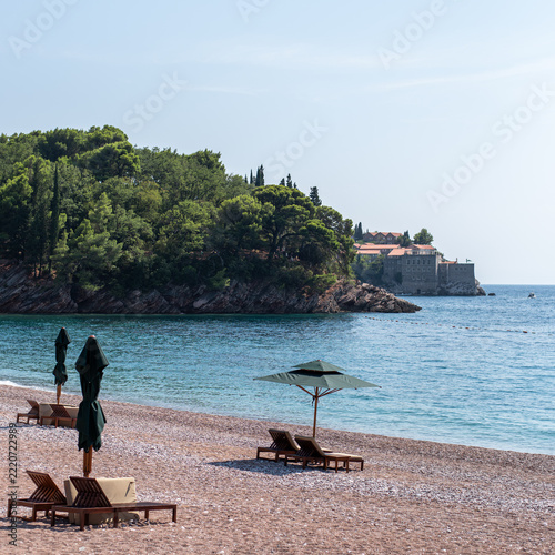 Sun loungers and parasols on a quiet pebble beach overlooking a calm blue bay