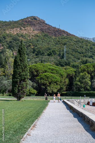 Couple in swimwear walks along a gravel path next to a green lawn with a mountain in the background