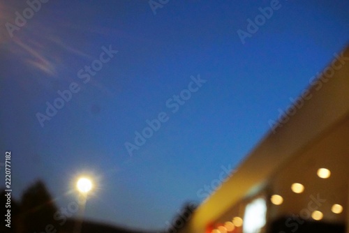 Abstraktes Motiv mit brauner großer Gebäudefassade, Flachdach und goldgelben Lichtern in Fensterreihen vor goldgelbem und Straßenlaterne und dunkelblauem Himmel in Stadt bei Nacht und  Nebel im Herbst