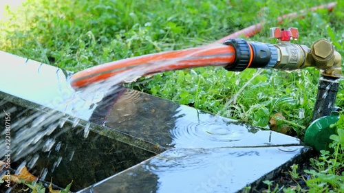 water leaking from garden hose connector on stone tile video screenshot, garden watering system hose pipe spraying water on lawn background, close up of water flowing from outdoor garden tap connector