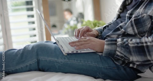 Hands landing on keys are initiating subject typing on white laptop on bed near blinds, studying