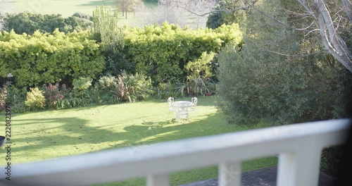 Balcony rail framing white table, 3 chairs are staying put as sunlight is shifting, casting shadows
