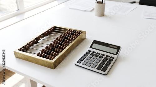 Antique brass abacus beside modern calculator on white office desk