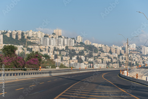 Empty highway curving toward Haifa cityscape on Mount Carmel hillside residential apartment buildings and urban architecture