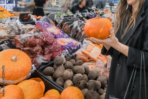 Woman choosing pumpkin among fresh vegetables in supermarket, autumn shopping and Halloween preparation