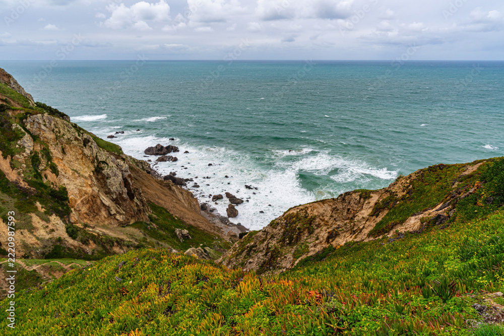 Fototapeta premium Cabo da Roca dramatic coastal cliff overlooking Atlantic Ocean in Portugal. Scenic westernmost point of Europe with rugged landscape, ocean waves and natural coastline.
