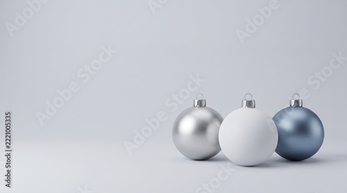 A minimalist Christmas arrangement featuring three spherical ornaments in metallic silver, matte white, and muted steel blue against a cool gray studio background.