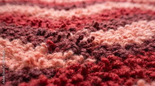 Knitted fabric with wavy stripes of red, pink, and burgundy yarn shows a soft texture.