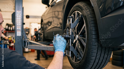 Professional mechanic performing wheel alignment service in repair garage focused on precision work for customer vehicle maintenance