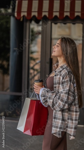 Young woman with long hair holding shopping bags and a coffee cup outside a boutique storefront