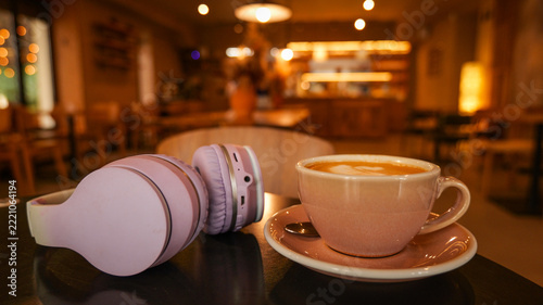 A warm cup of latte with latte art sits beside wireless headphones on a cafe table at night