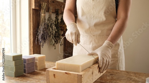 Soap maker drawing a thin wire down through a block of pale handmade soap to cut an even slice in a bright workroom
