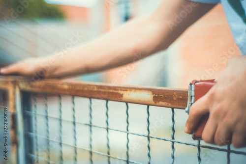 Close-up of hands using a sanding block to smooth a rusty metal fence before painting. Motion blur adds a raw, authentic feel. DIY restoration photo for craft and renovation projects