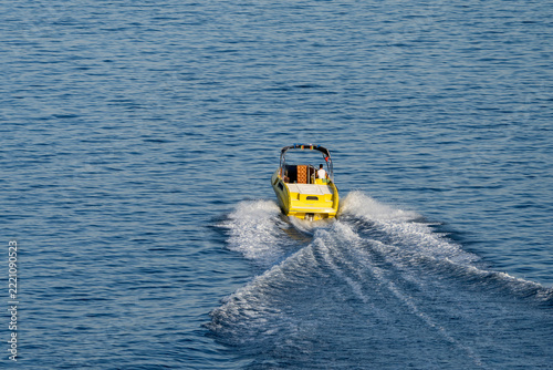 Yellow speed boat speeding away on open sea leaving white foam wake