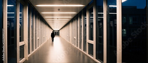 Lone man walking in modern glass corridor at night