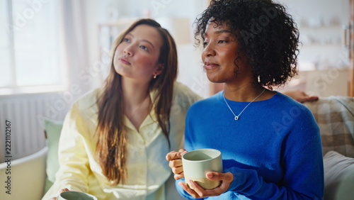 Multiracial women sharing coffee sofa. Two friends talking heartfelt home.