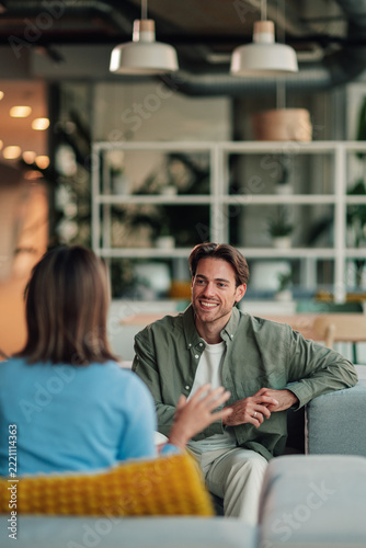 Young man smiling and communicating with a woman in an informal office meeting, discussing business in a modern workplace