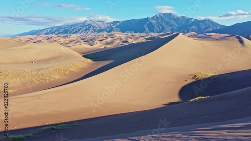 Expansive sand dunes stretch toward distant mountain peaks under clear morning skies in Great Sand Dunes National Park
