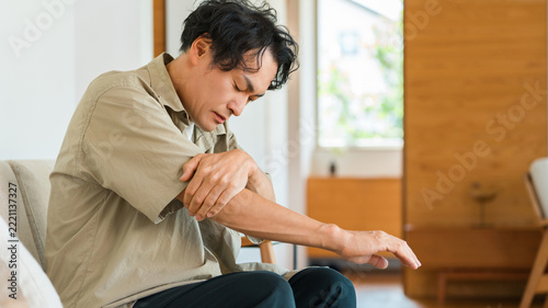 家で肘を押さえて腕の痛みに悩む40代男性。肘関節の痛みや筋肉疲労・体の不調のイメージ