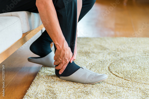 A man in his 40s at home holding his ankle, an image of suffering from ankle pain, sprain, and joint pain