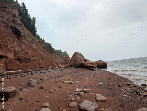 Red sandstone sea cliffs and fallen boulders on beach on September 3, 2026 in Quebec, Canada