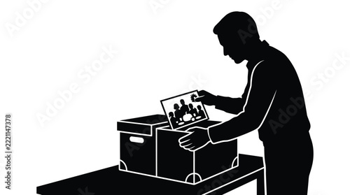 Black silhouette of man looking at old family photograph while packing belongings into boxes