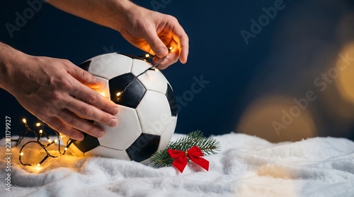 Hands decorating a soccer ball with christmas lights on snow for a