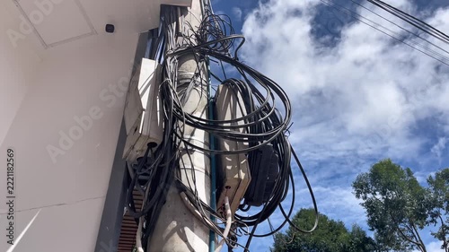 Close-up of urban telecommunications infrastructure and electricity network. Messy overhead power lines, bundled fiber optic cables, and utility internet wires attached to a concrete pole