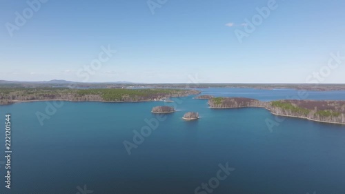 High angle panoramic footage over a wide blue freshwater lake dotted with scenic green forested islands and quiet shores under a clear bright sky on a sunny summer day