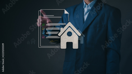 Businessman approves mortgage loan agreement with virtual house and checklist document, symbolizing property investment, real estate insurance, and home purchase deal.