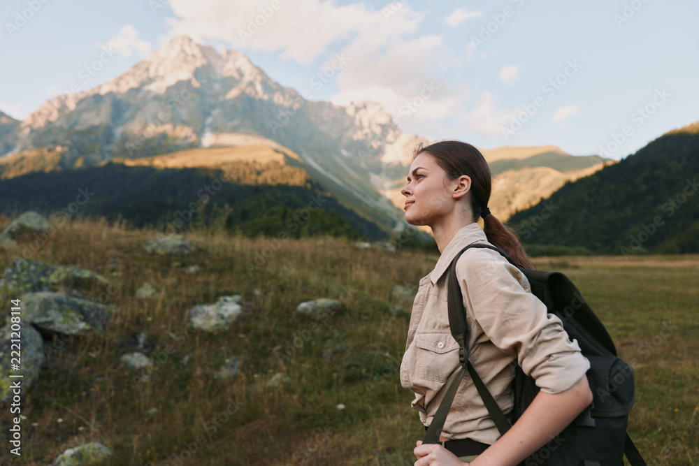 Naklejka premium A woman hiking with a backpack in an open valley, mountains in the background, capturing a moment of outdoor exploration and scenic nature.