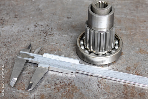 Stainless steel vernier caliper measuring spline shaft with ball bearing on metal surface.