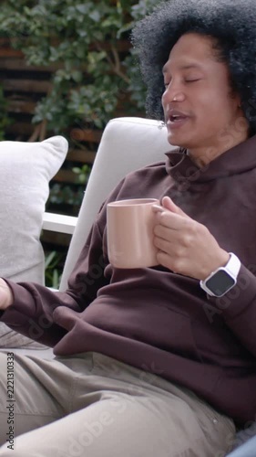 Vertical video: Reacting to partner speaking, man in hoodie holding pink mug and gesturing on patio