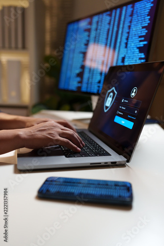 Cybersecurity professional accessing a secure login interface on a laptop, with digital code on a monitor, representing data protection and online privacy.