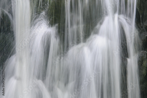 Fotografie Close detail of a waterfall where long exposure turns the falling water into soft white veils over dark rock