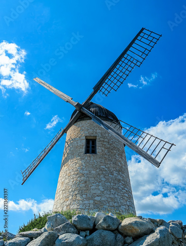 Old traditional stone windmill with wooden blades against blue sky