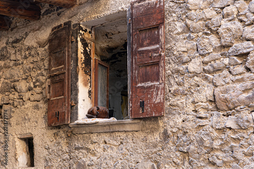 Old open rustic window with weathered wooden shutters and a hand carved wooden sleeping cat figurine on the stone sill in Canale di Tenno, Italy.