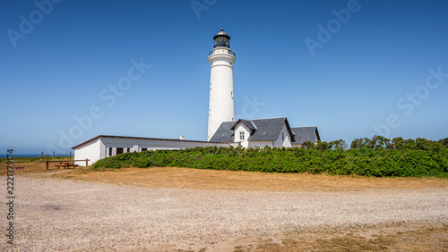 Scenic view of the historic white Hirtshals Fyr lighthouse and surrounding keeper houses in Denmark standing on a grassy field under a clear blue sky on a sunny summer day