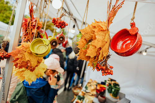 Autumn decorations featuring golden maple leaves, red berries, and colorful hanging ceramic bowls displayed at a market stall