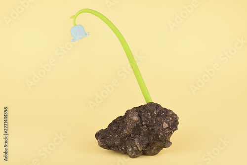 Artificial plastic flower growing out of a stone on a yellow background. Concept of resilience, survival and hope.